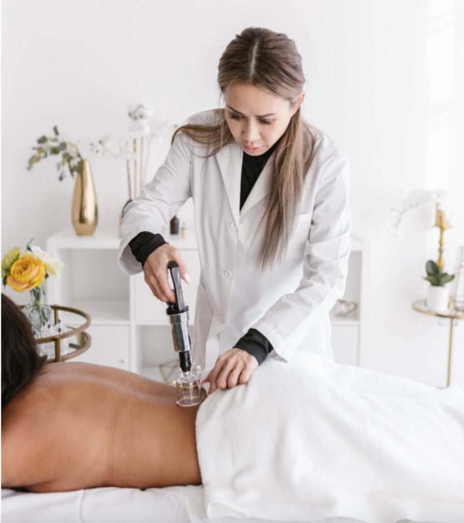 a woman in a while lab coat using a suction utensil to do cupping therapy on the lower back region of a patient